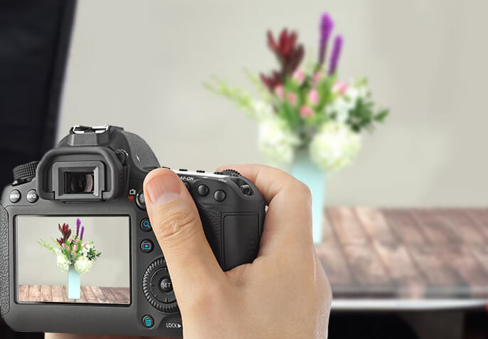 Hand-held camera focused on floral arrangement, with arrangement also displayed in camera view-finder.